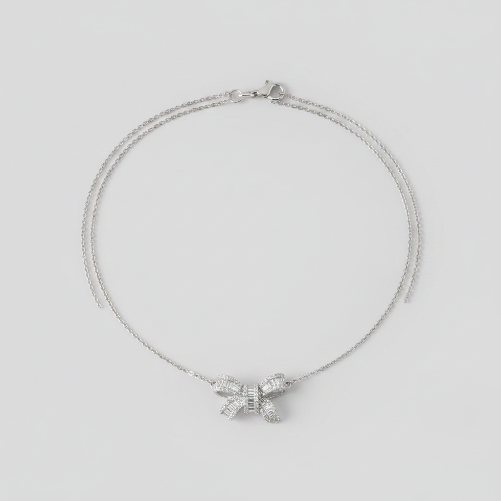 Silver bow shaped necklace on a person's neck against a neutral background