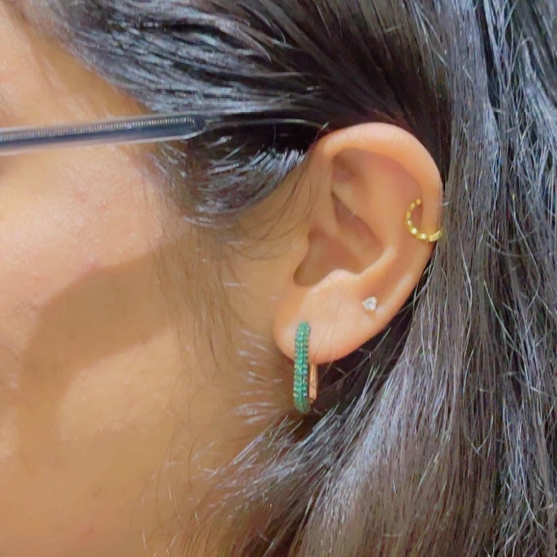 Close up of an ear with multiple earrings including a gold hoop, green hoop, and silver stud
