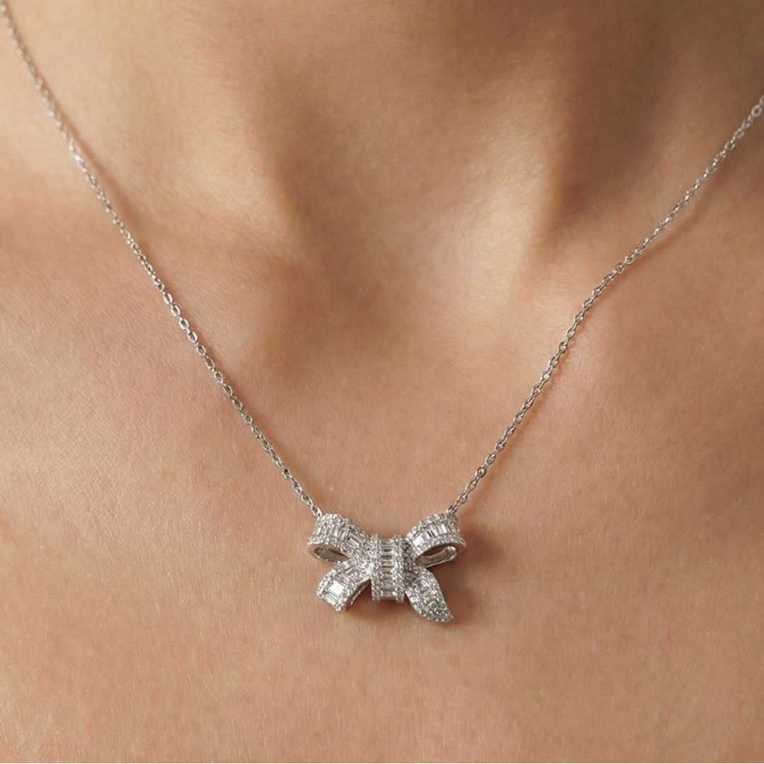 Silver bow-shaped necklace on a person's neck against a neutral background