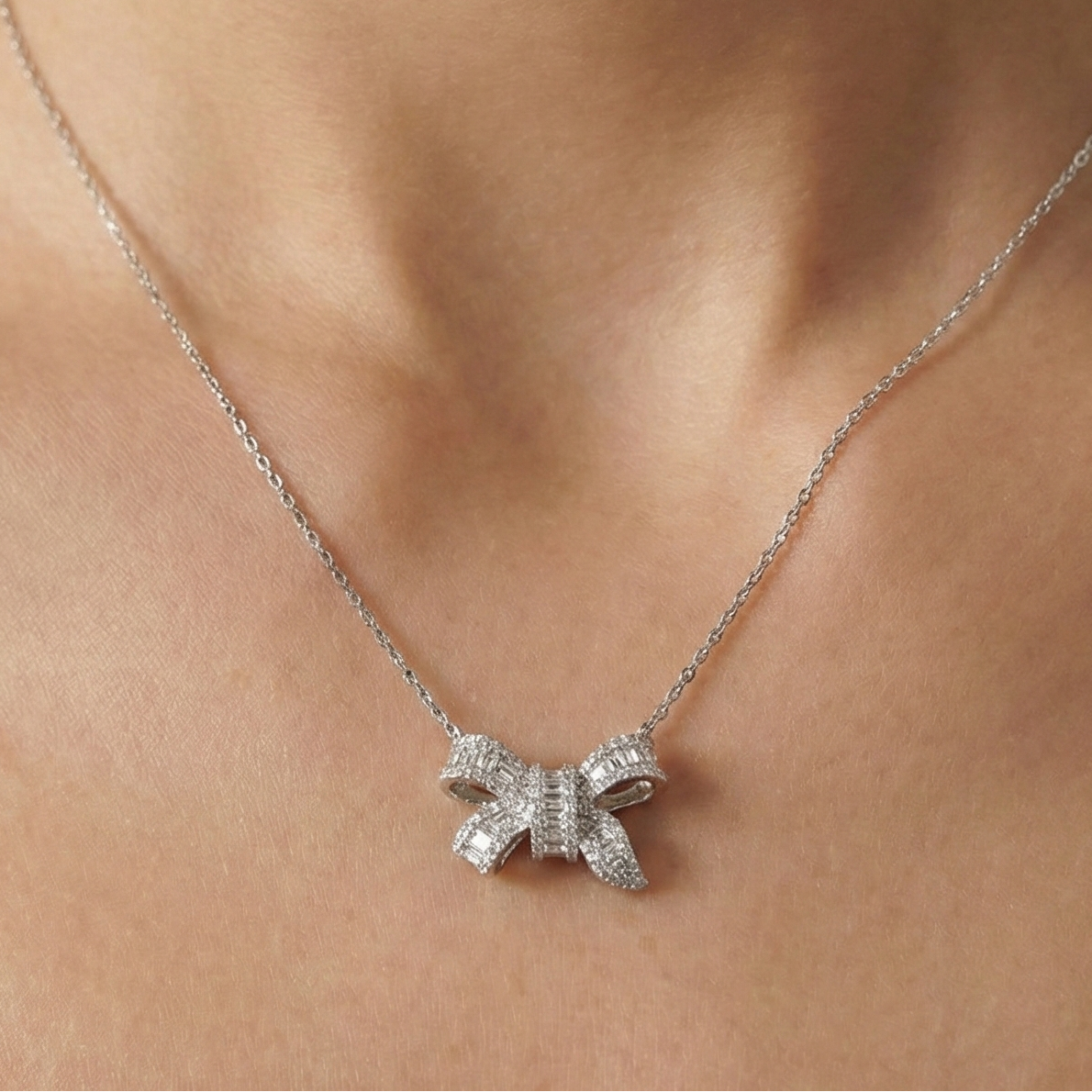 Silver bow shaped necklace on a person's neck against a neutral background